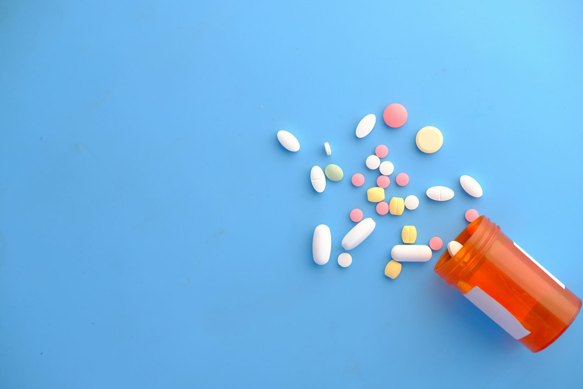 colourful pills spilling out of an orange bottle